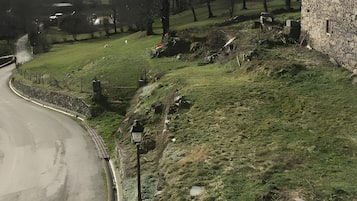 Ländliche Landschaft mit einem Steinhaus, einer kurvenreichen Straße und einem Bergpanorama im Hintergrund.