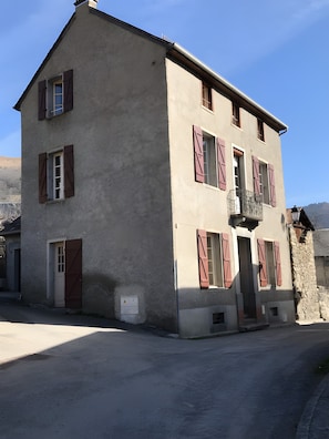 A two-story building with a balcony, a door, and a window with shutters.