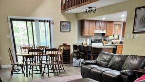 A spacious living room with a leather sofa, a dining area with wooden chairs, and a kitchen in the background. - 3-bedroom house in superb Big Bass Lake with AC (Big Bass Lake)