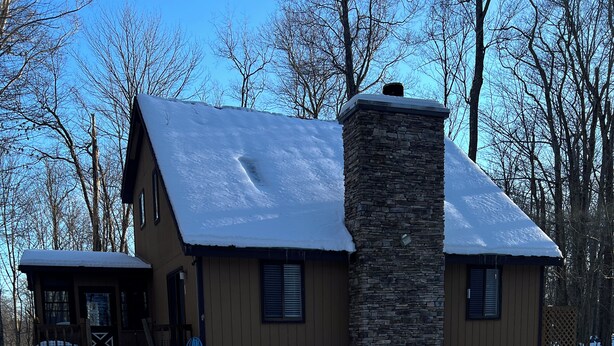 A two-story house with a stone chimney, wooden siding, and a snow-covered roof. - 3-bedroom house in superb Big Bass Lake with AC (Big Bass Lake)