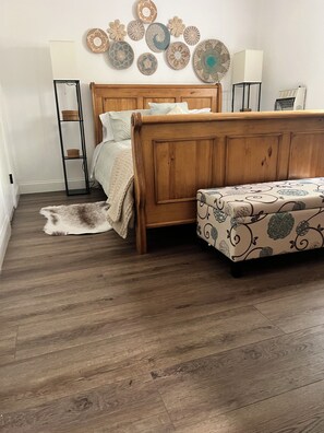 Quarto com cama de madeira, um banco, tapete de pele, luminária na parede e pratos decorativos.