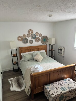 Quarto com cama de madeira, luminária de cabeceira, aquecedor na parede e pratos decorativos.
