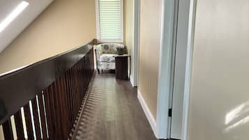 Un couloir avec une rambarde en bois, un banc agrémenté d’une plante et une porte sur la droite.