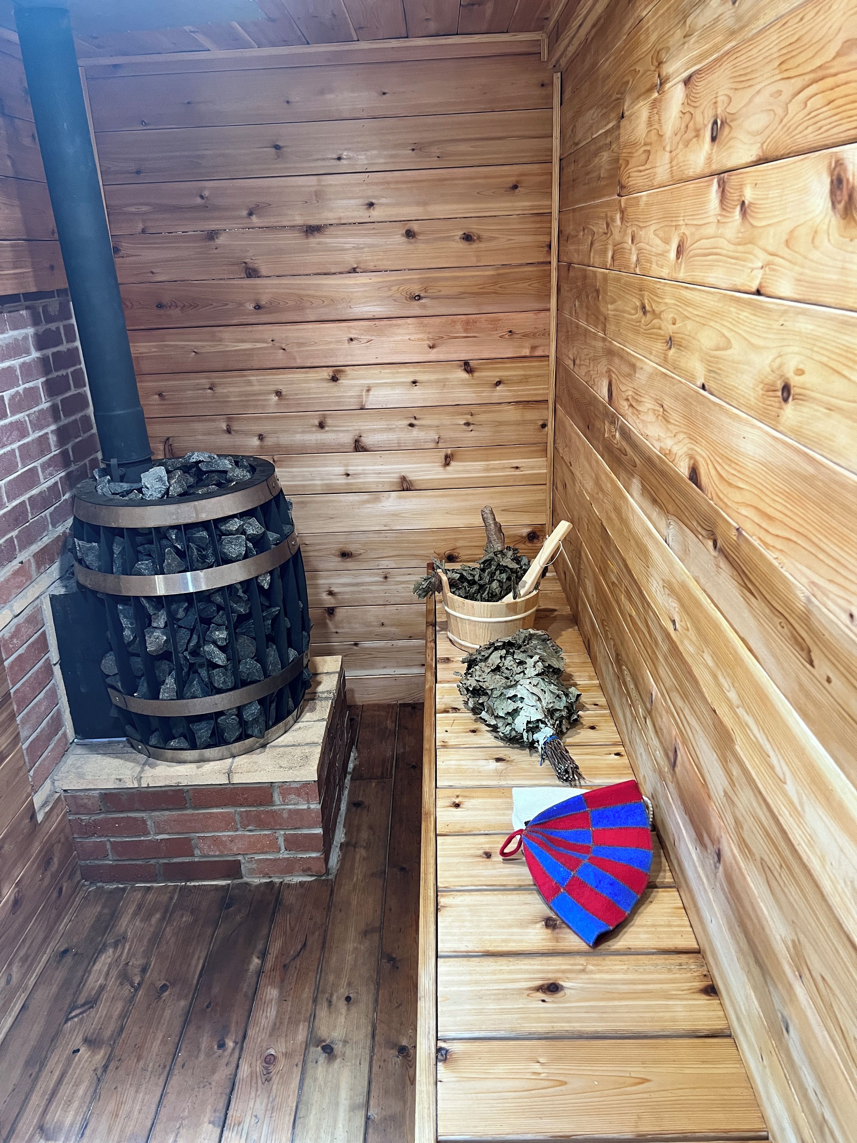 Een houten hutje interieur met een houtkachel, een bank en een mand vol haardhout.