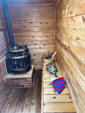 A wooden cabin interior with a wood-burning stove, a bench, and a basket of firewood.