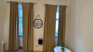 Una stanza con tende color crema, un quadro appeso alla parete, un tavolino con una pianta e un termosifone.