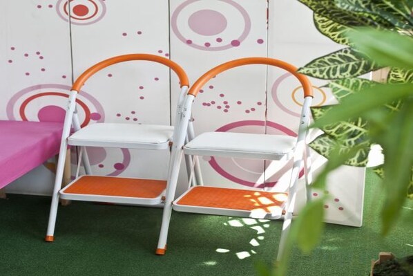 Two white chairs with orange accents, a green floor, and a wall with circular patterns. - Ari House (Seoul)