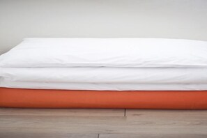 Un lit bien fait, avec une literie blanche et orange.