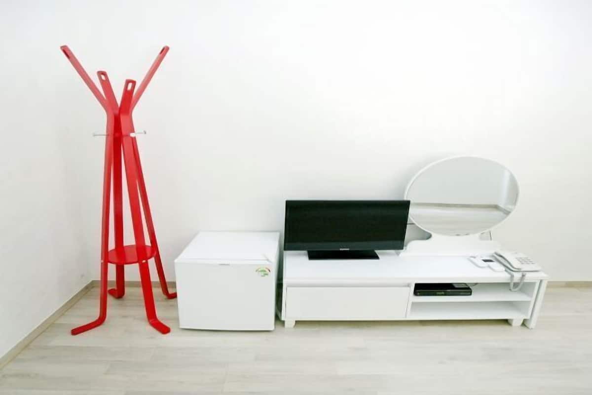 A white desk with a flat-screen TV, a mirror, and a telephone.