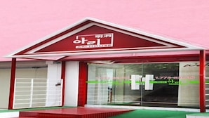 A building with a red and white facade, a glass entrance, and a green carpeted area in front.