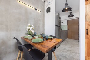 Un coin repas avec une table en bois dressée pour quatre personnes, des chaises noires et un vase contenant des fleurs blanches.