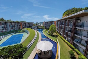 Een modern hotel met meerdere verdiepingen, tennisbanen buiten, een zwembad en weelderige beplanting.