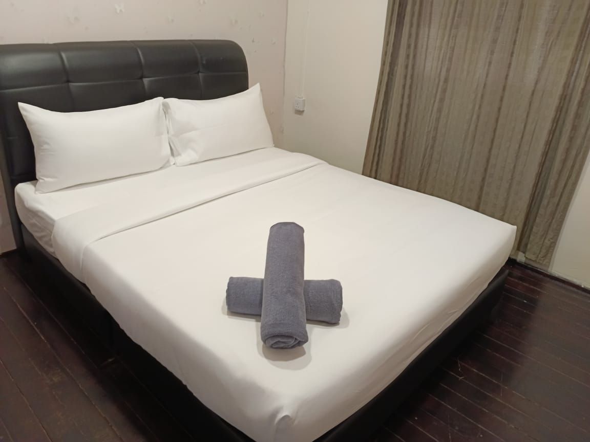 A neatly made bed with white linens and a rolled gray towel in the center.