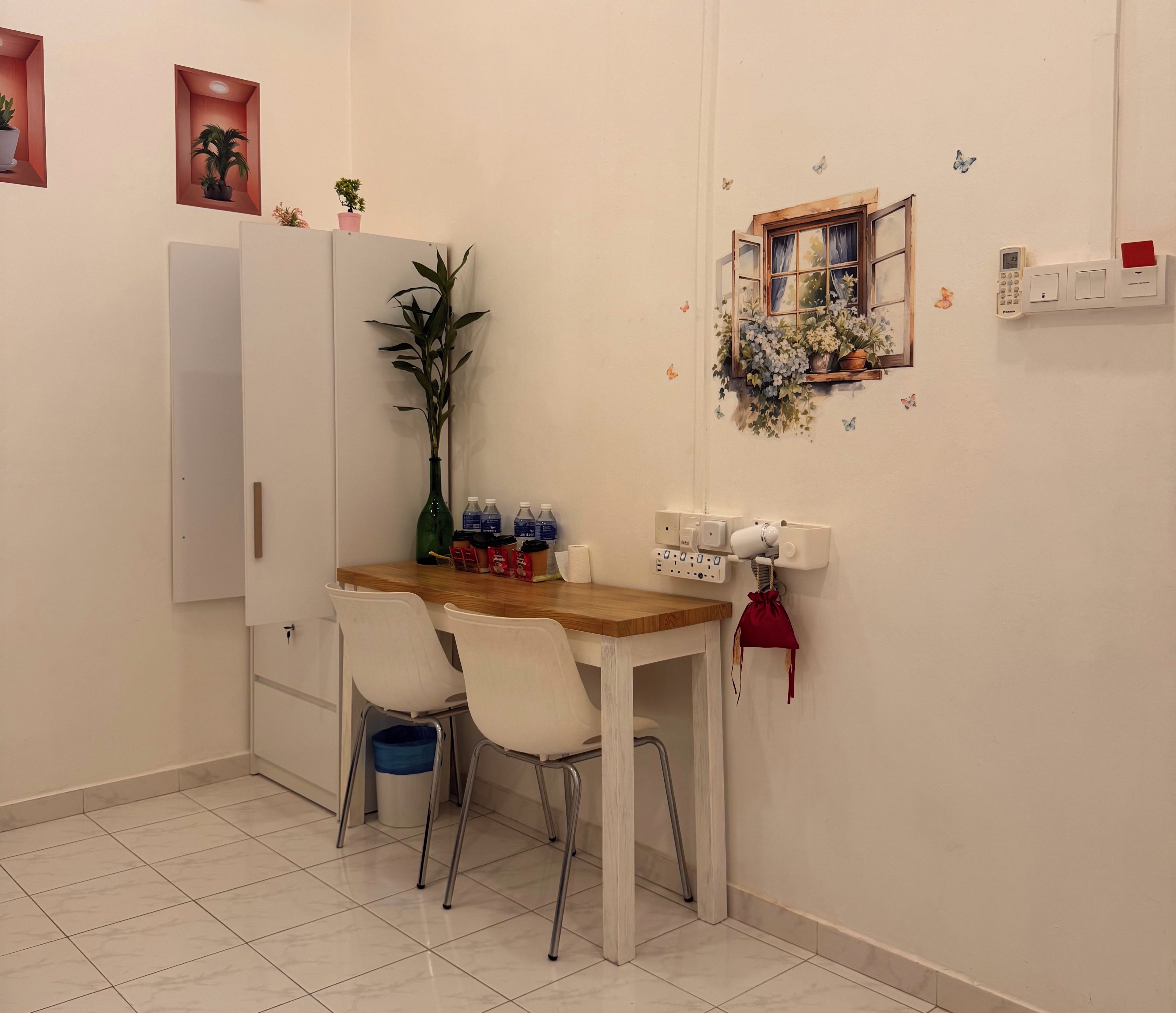 Un'angolata da pranzo con tavolo in legno, due sedie bianche, un vaso con una pianta e una mensola a muro con fiori.