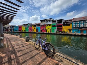 A canal with colorful buildings on one side and a bicycle parked by the water. - The Backpackers Hut @ Jonker Melaka (Malacca City)