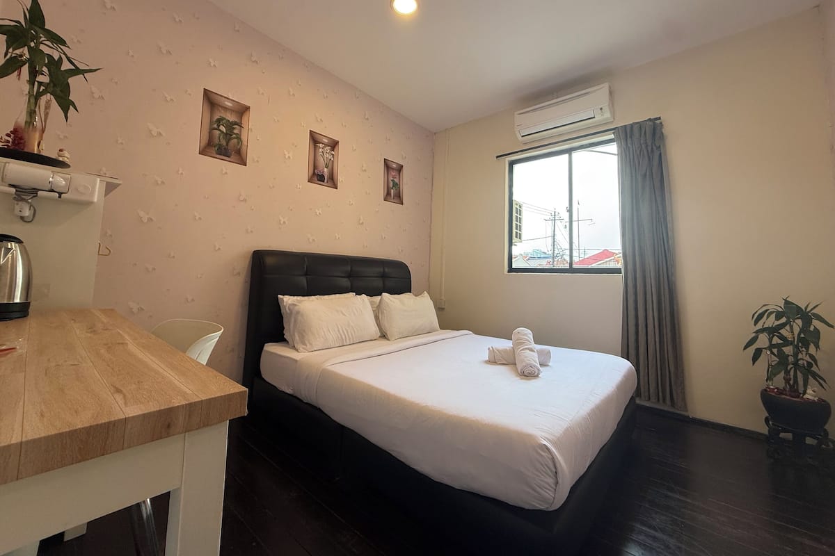 Hotellihuone, jossa on sänky, työpöytä, tuoli, ruukkukasvi ja ilmastointilaite.