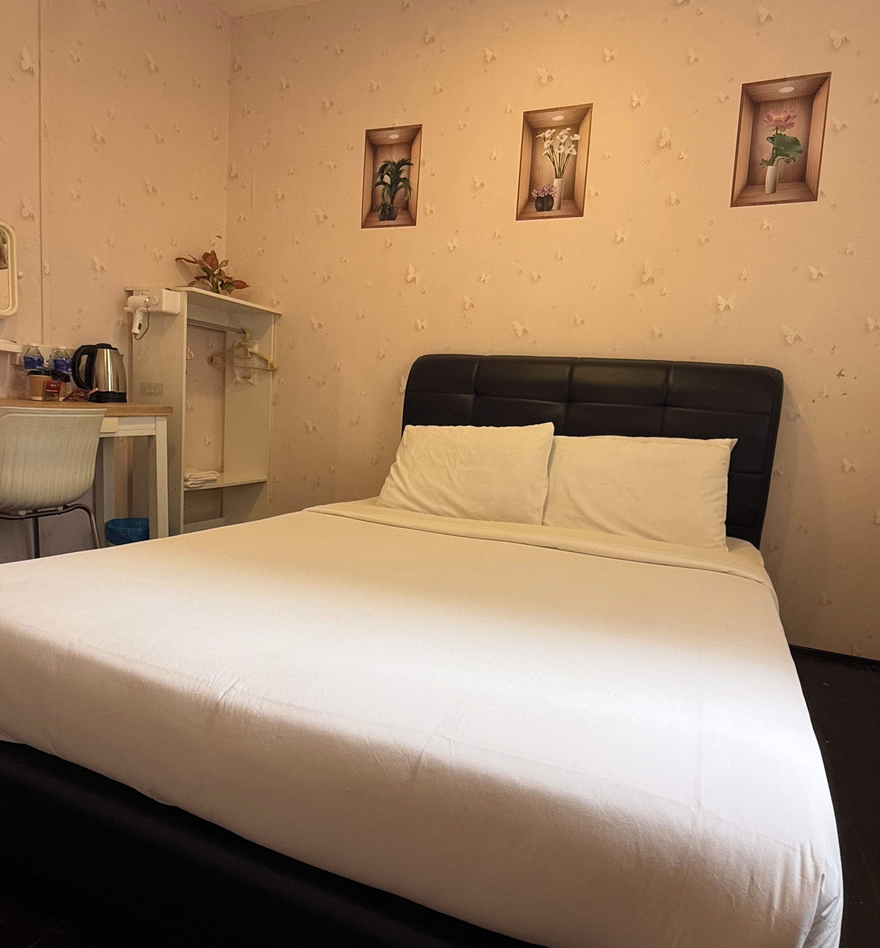 A neatly made bed with white linens, a small desk with a chair, and three wall-mounted shelves with decorative items.