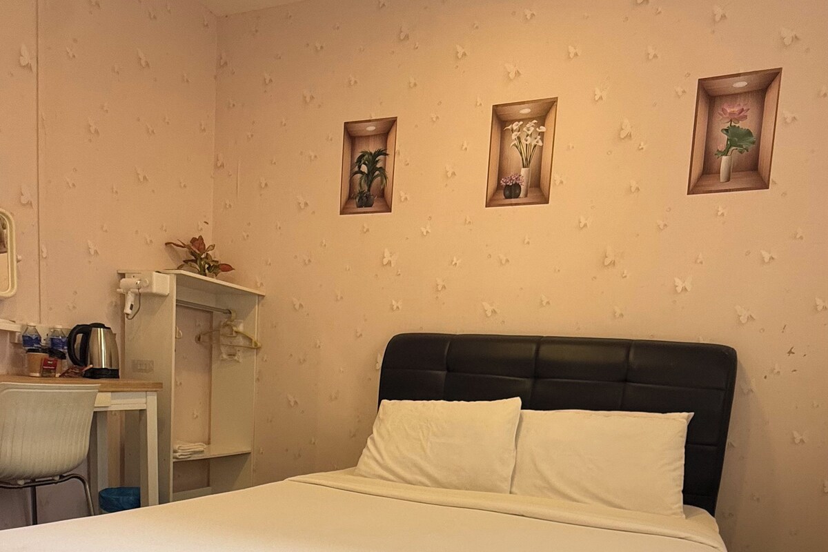 A neatly made bed with white linens, a small desk with a chair, and three wall-mounted shelves with decorative items.