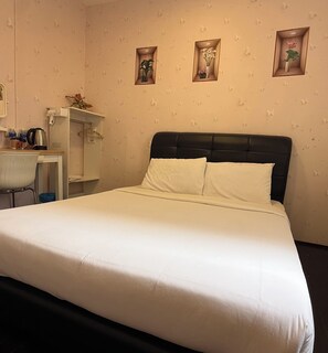 A neatly made bed with white linens, a small desk with a chair, and three wall-mounted shelves with decorative items.