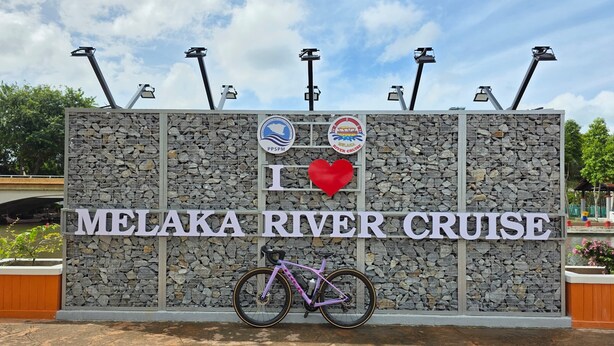 A sign for Melaka River Cruise with a bicycle parked in front. - The Backpackers Hut @ Jonker Melaka (Malacca City)