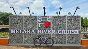 Señal para el paseo en barco por el río Melaka, con una bicicleta estacionada al frente.
