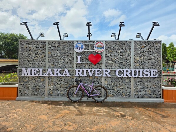 A sign for Melaka River Cruise with a bicycle parked in front. - The Backpackers Hut @ Jonker Melaka (Malacca City)