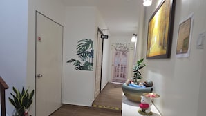 Een gang met een houten vloer, een witte deur met een 'verboden toegang'-bord, een plant, een wandlamp en een ingelijst beeld.