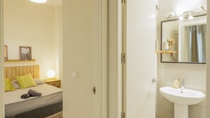 Et hotelværelse med seng, natbord, lampe og et badeværelse med vask og spejl.
