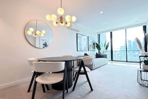 A modern living room with a round dining table, a sofa, and a large window with a city view.