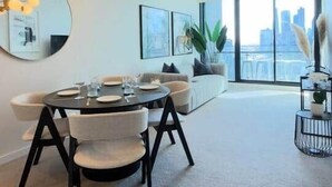 A modern dining area with a round table, chairs, and a chandelier. There is a large mirror on the wall and a sofa in the background. - Luxury apartment & free parking x1 (Southbank)