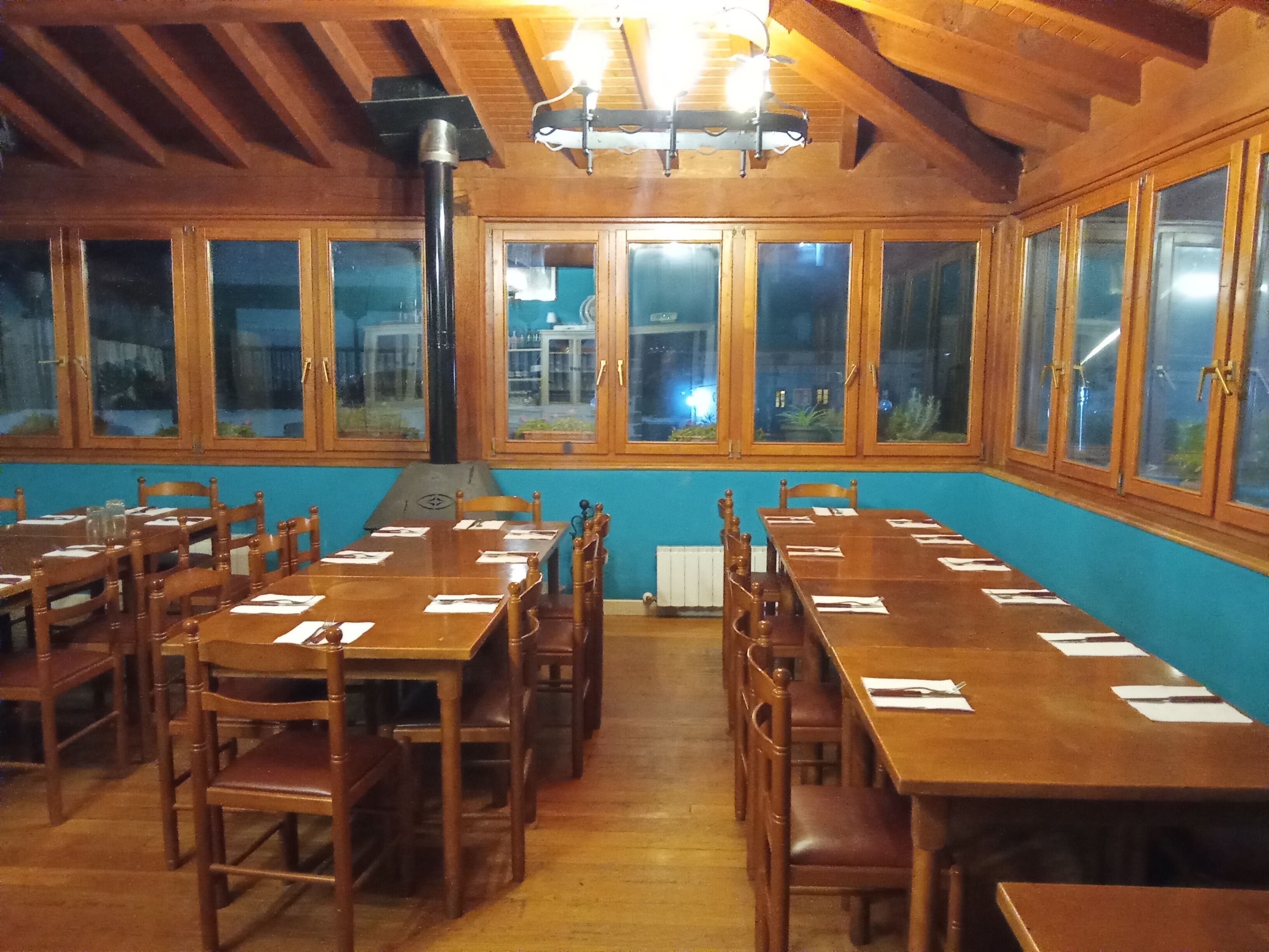 A dining hall with wooden tables and chairs, large windows, and a high ceiling with exposed beams.