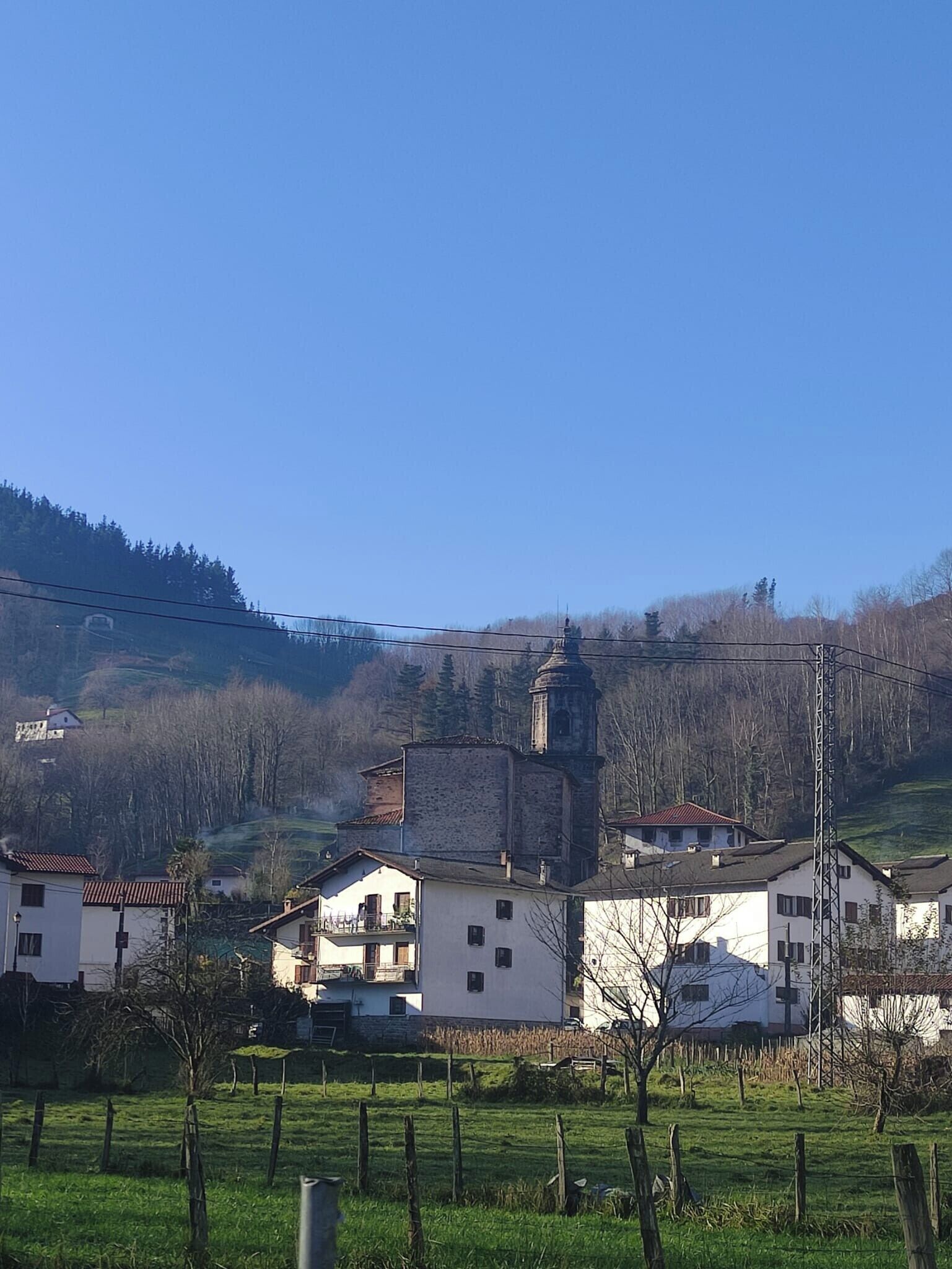 Un pueblo rural con casas blancas tradicionales, una iglesia y una colina al fondo.