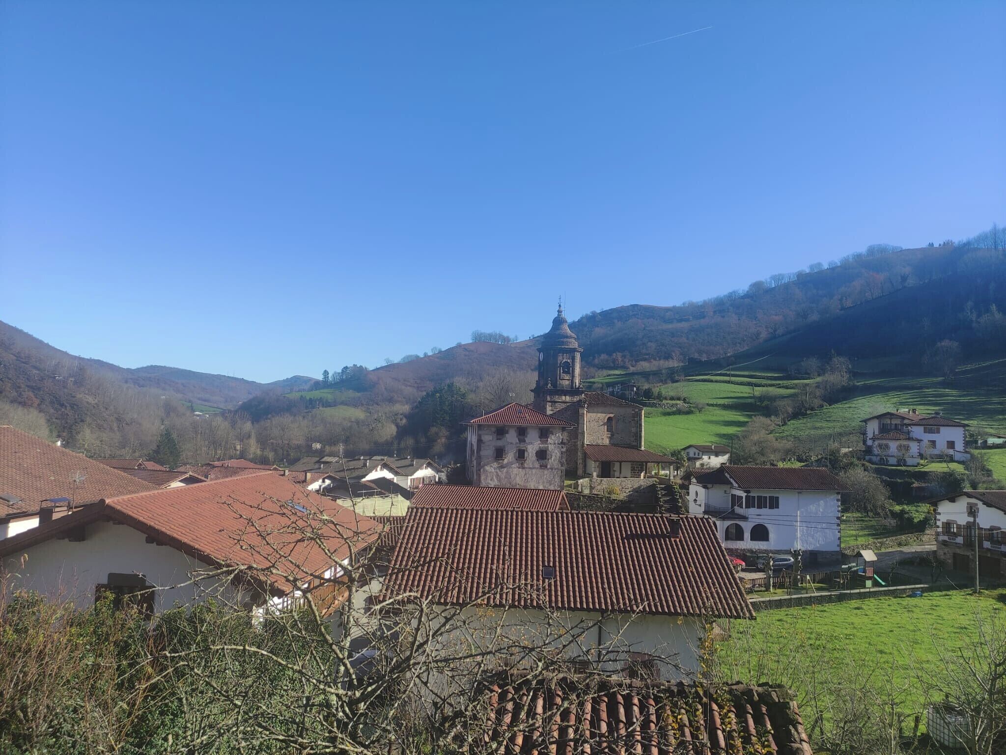 A rural village with traditional architecture, including a prominent church with a bell tower, surrounded by houses with red-tiled roofs.