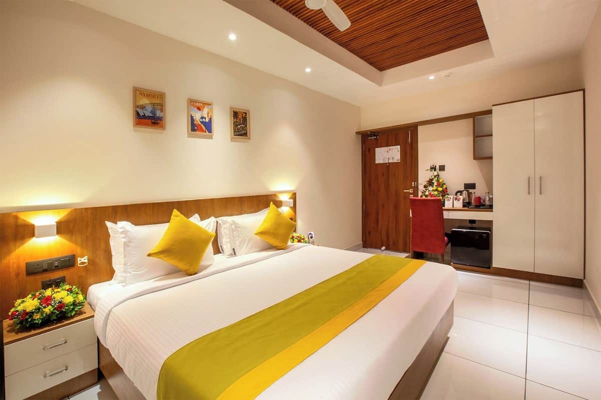 A hotel room with a large bed, wooden headboard, bedside tables with lamps, a red chair, a kitchenette, and a wardrobe.