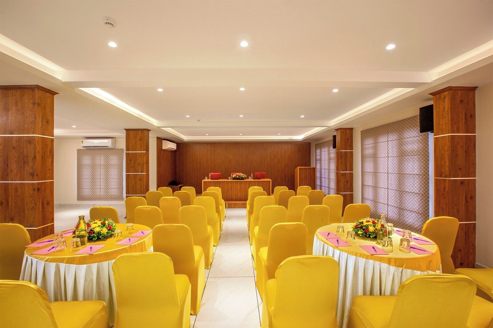 A conference room with yellow chairs and tables, wooden paneling, and a stage with a red podium.