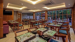 Ένα εστιατόριο με ξύλινα τραπέζια και καρέκλες, μεγάλα παράθυρα και ένα μοντέρνο σχέδιο στην οροφή.