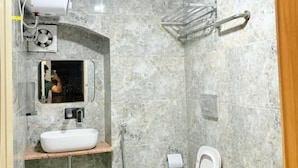 A modern bathroom with a marble floor, a built-in sink, a toilet, and a shower area. - Hotel Mangalam (Varanasi)