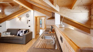 Een zolderkamer met een houten plafond, een bank, een wastafel en een raam.