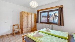 Een kamer met twee bedden, een houten garderobe, een stoel en een raam met gordijnen.