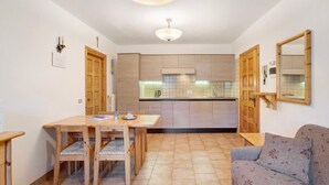 Een kleine keuken met houten kastjes, een eettafel met stoelen, een bank en een plafondlamp.