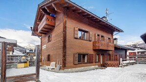 Een houten chalet met een balkon, een skilift en een besneeerd landschap.