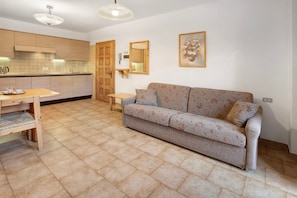 A modern kitchen with wooden cabinets, a dining table with chairs, a sofa, and a small table.
