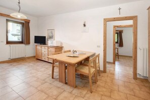 Un comedor con una mesa y sillas de madera, televisor, microondas y una ventana con cortinas.