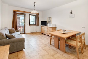 A living room with a sofa, a dining table with chairs, a television, and a cabinet.