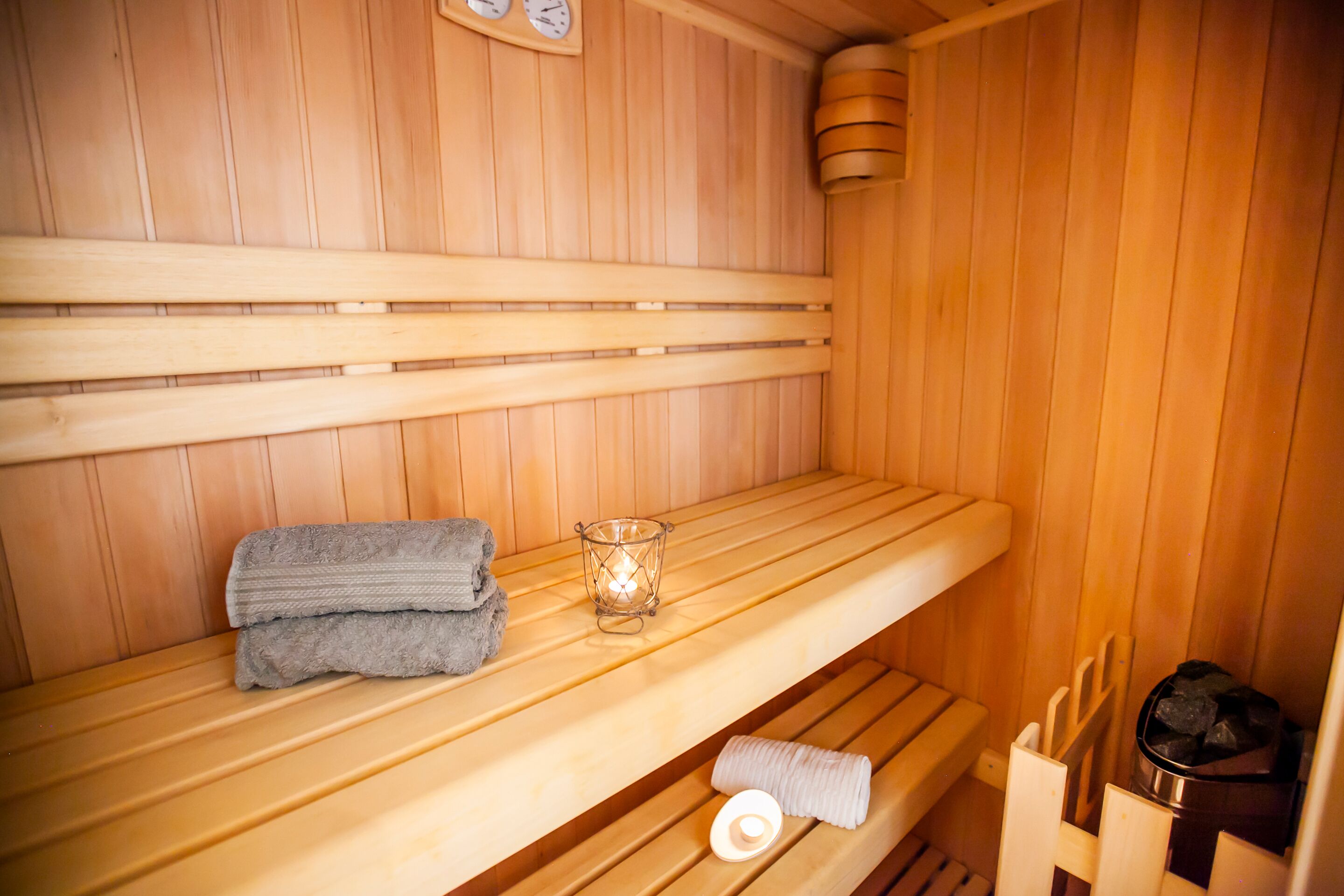 Uma sauna de madeira com bancos, uma vela de vidro e toalhas.