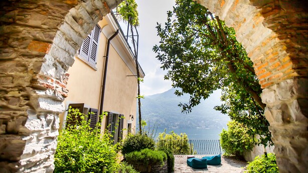 An arched stone doorway leading to a courtyard with a view of a lake and mountains. - Appartamento Fioravante by Wonderful Italy (Moltrasio)