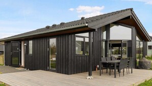A modern wooden house with a large deck, sliding glass doors, and a dining area. - 5 Star Holiday Home in Horve (Ronde)