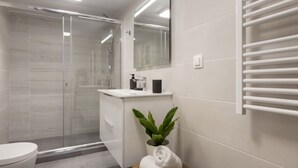 A modern bathroom with a glass shower enclosure, a white sink, a mirror, a towel rack, and a potted plant. - Pausaniou 8 studio-Eclectic Studio near Kal (Athens)