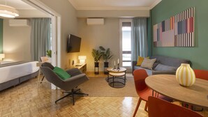 A modern living room with a sofa, armchair, dining table, and a TV mounted on the wall. - Pausaniou 8 studio-Eclectic Studio near Kal (Athens)
