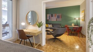 A modern living room with a wooden floor, a desk with a chair, a sofa, and a dining area with chairs and a table. - Pausaniou 8 studio-Eclectic Studio near Kal (Athens)